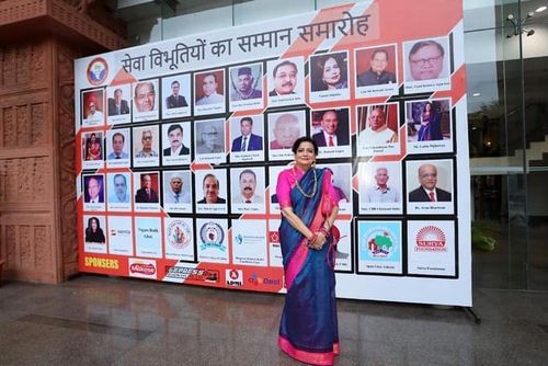 Mrs. Lalita Nijhawan standing in front of award hoarding